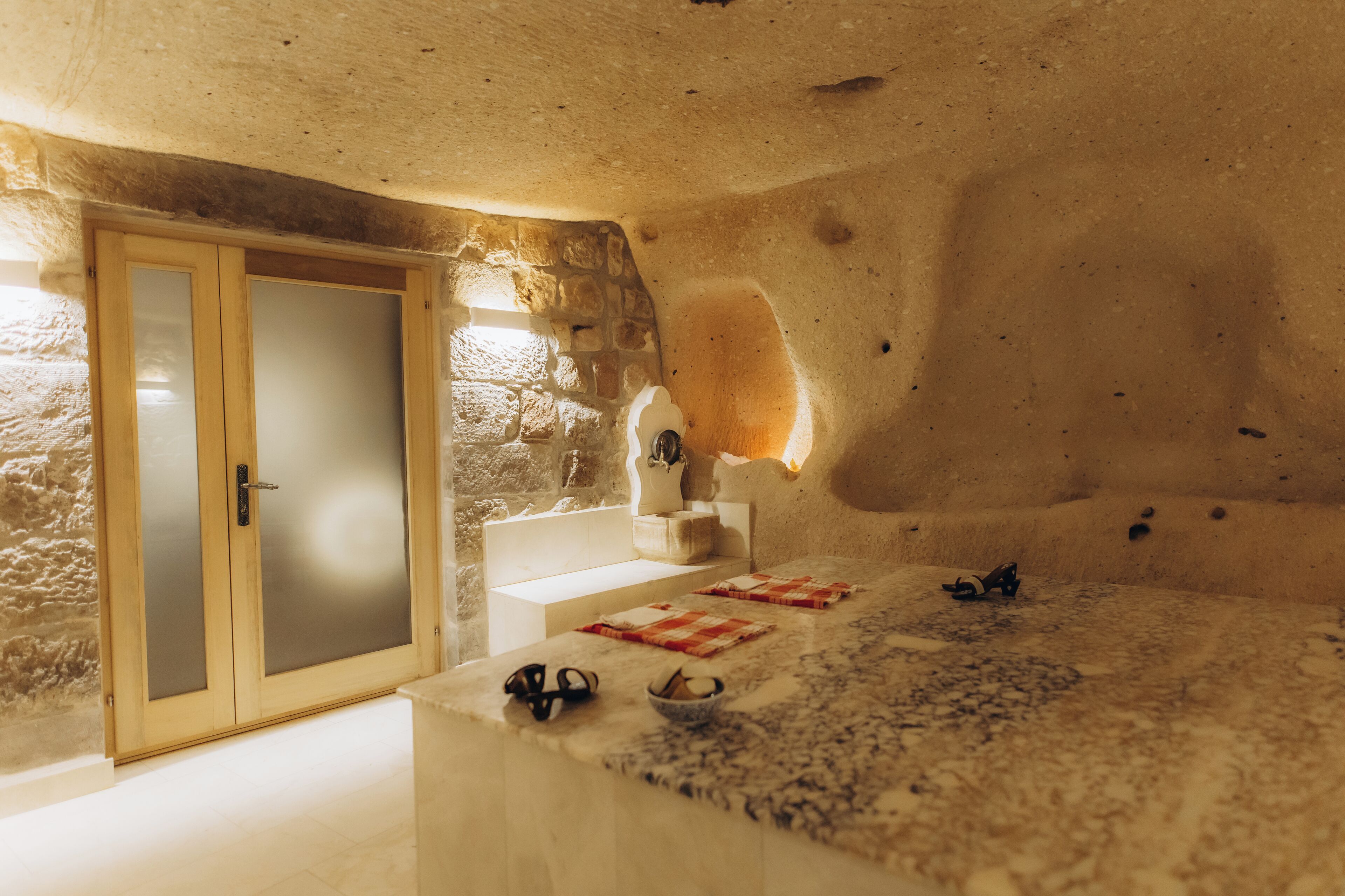 A room with a stone wall, a wooden door with frosted glass panels, a marble countertop, and a small table with a bowl and utensils.