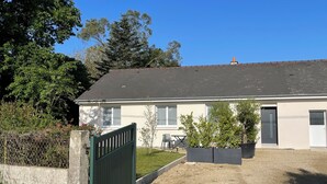 Una casa de un piso con techo oscuro, un pequeño porche y un patio cercado.