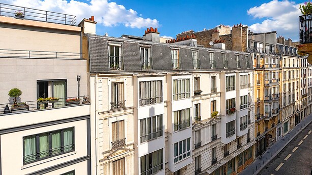 A row of multi-story buildings with balconies, large windows, and a clear blue sky. - L'appartement Bouquet  (Paris)