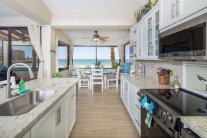 A kitchen with a view of the beach, a dining area, and a ceiling fan.