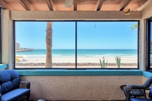 A room with a large window overlooking a beach, two wicker chairs, and a view of the ocean.