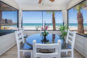 A round table with chairs, a vase with flowers, and a view of the beach and ocean.