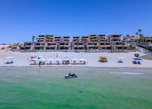A beachfront hotel with multiple balconies, beach umbrellas, and a clear view of the ocean. - Super Beachfront Condo Ground Level on Sandy Beach (Puerto Peñasco)