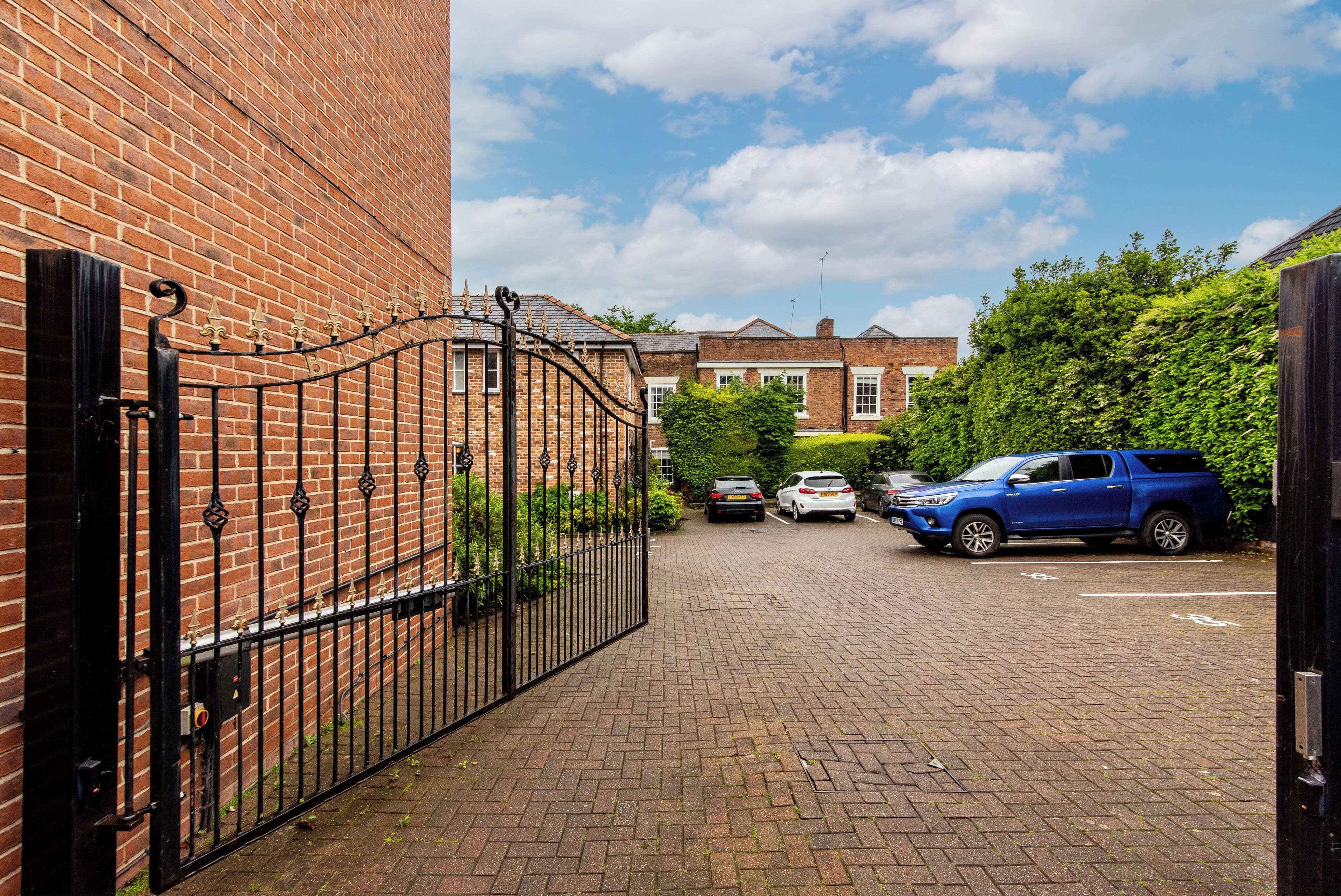 Un edificio de ladrillo con un camino de entrada cerrado y coches aparcados.