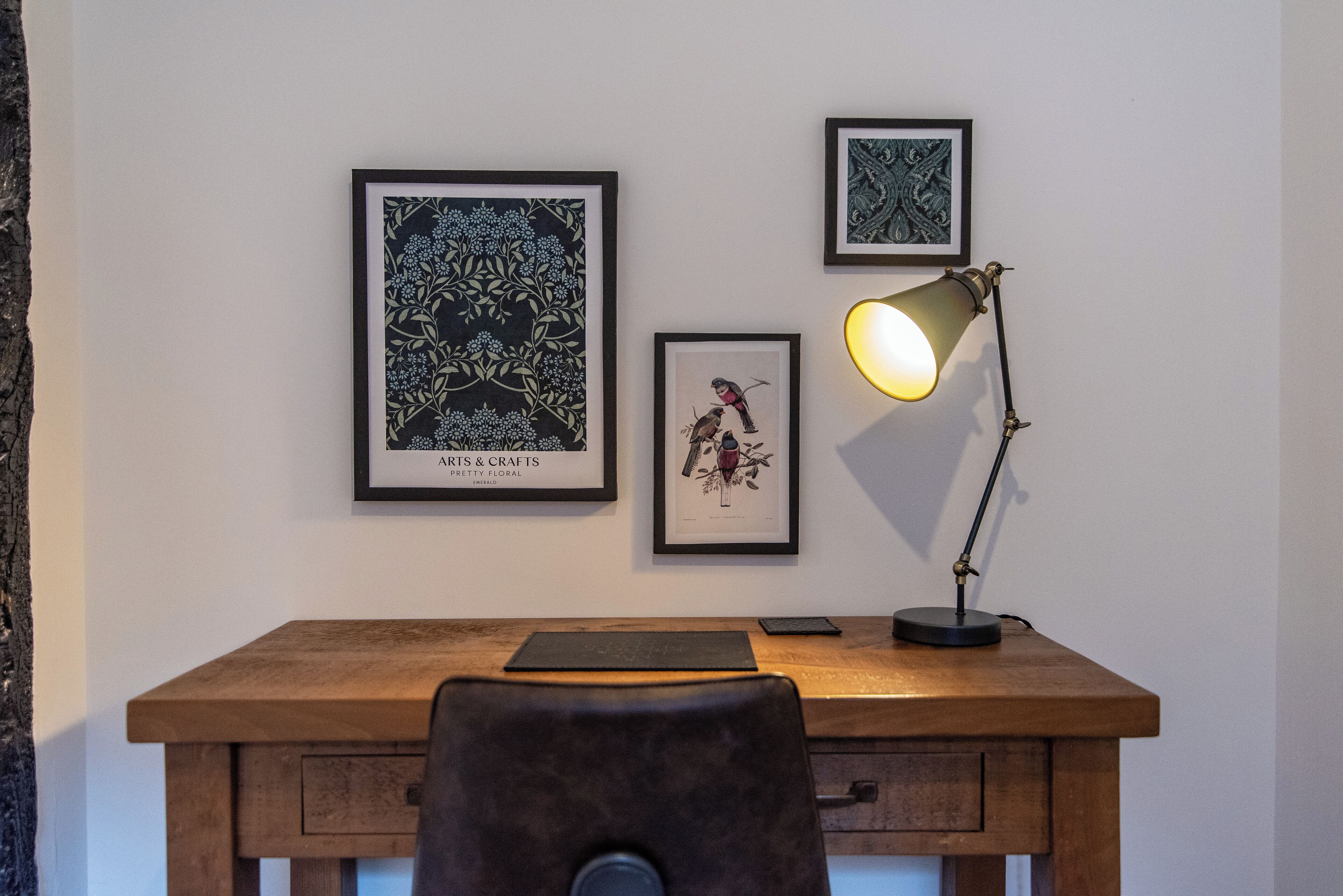 Ein Holztisch mit einer schwarzen Lampe, zwei gerahmten Kunstwerken und einem Smartphone darauf.