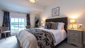 Een slaapkamer met een groot bed, een nachtkastje met lampen, een stoel en een raam met gordijnen.