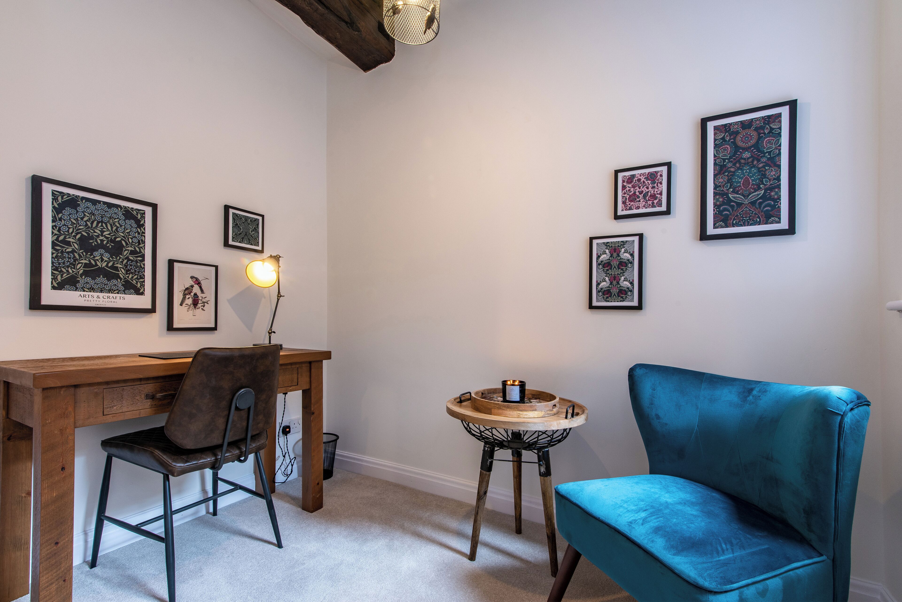 A room with a wooden desk, a blue chair, and a small round table with a candle.