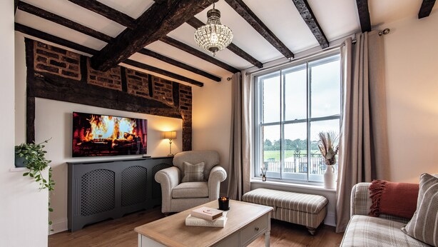 Een gezellige woonkamer met een open haard, een televisie, een comfortabele bank en een groot raam met gordijnen.