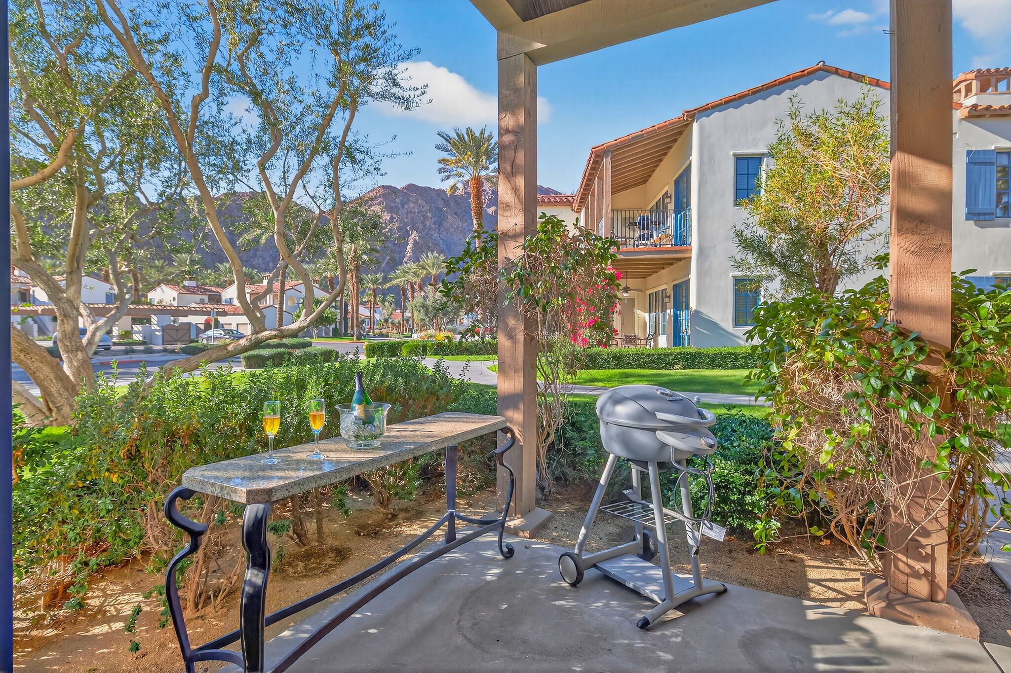 Une terrasse extérieure avec un barbecue, une table avec des boissons et une vue sur une montagne et des immeubles résidentiels.