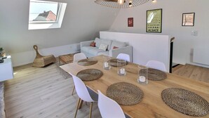 A modern living room with a wooden dining table, white chairs, a white sofa, and a ceiling fan. - Charming 3-bedroom house in the vineyard with terrace (Vœgtlinshoffen)