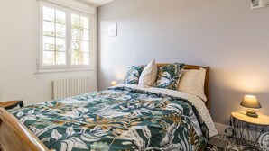 A bedroom with a bed, a window, a radiator, a bedside lamp, and a small table with a lamp. - Single-story house with garden and parking in Yvetot-Bocage (Yvetot-Bocage)