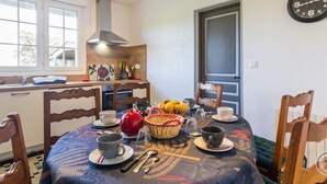 A dining area with a table set for four, a clock on the wall, and a window with blinds. - Single-story house with garden and parking in Yvetot-Bocage (Yvetot-Bocage)