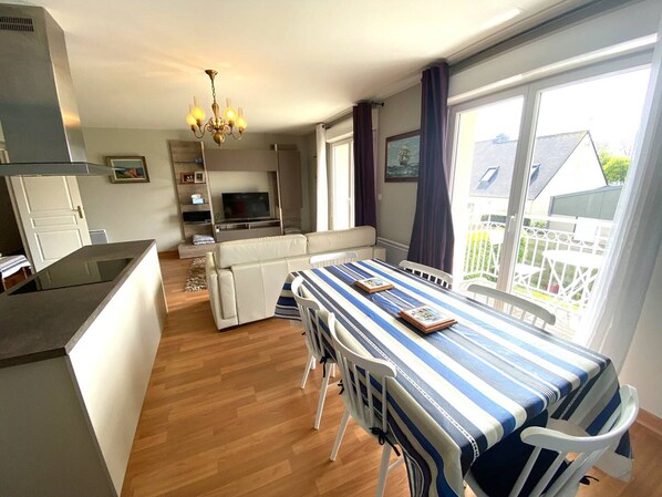 A modern kitchen with a built-in oven, a dining area with a striped tablecloth, and a large window with a view of the outside. - Centrally Located Perros-Guirec Apartment with WiFi, Balconies, and Parking (Perros-Guirec)