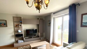 Ein modernes Wohnzimmer mit Flachbildfernseher, einer Couch, einem Couchtisch und einer Deckenleuchte.