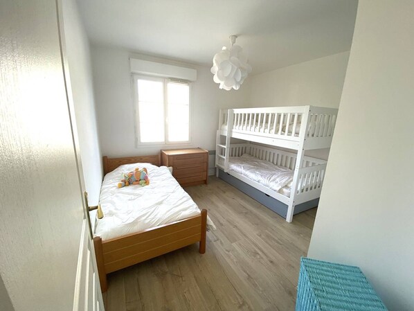 A bedroom with a wooden bed, a bunk bed, a window, and a small wooden nightstand.