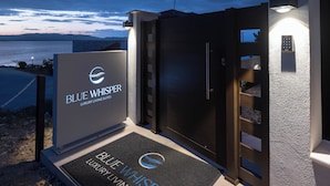 Een omheind toegangshek naar Blue Whisper Luxury Living Suites, met een helder zicht op het omliggende landschap.