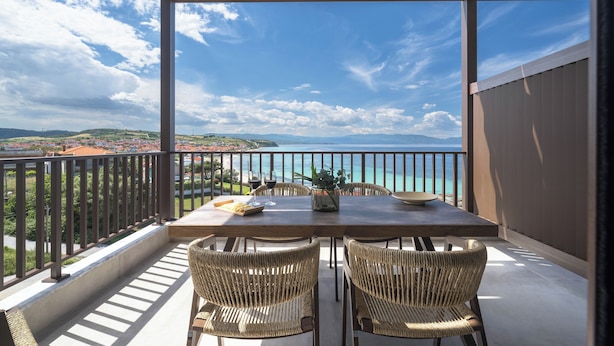 Een balkon met een tafel en stoelen, met uitzicht op de kust.