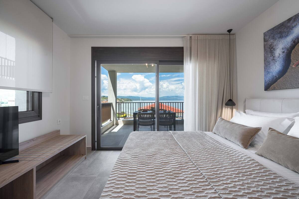 Een moderne hotelkamer met een groot bed, een televisie, een balkon met uitzicht op de bergen en een schilderij aan de muur.