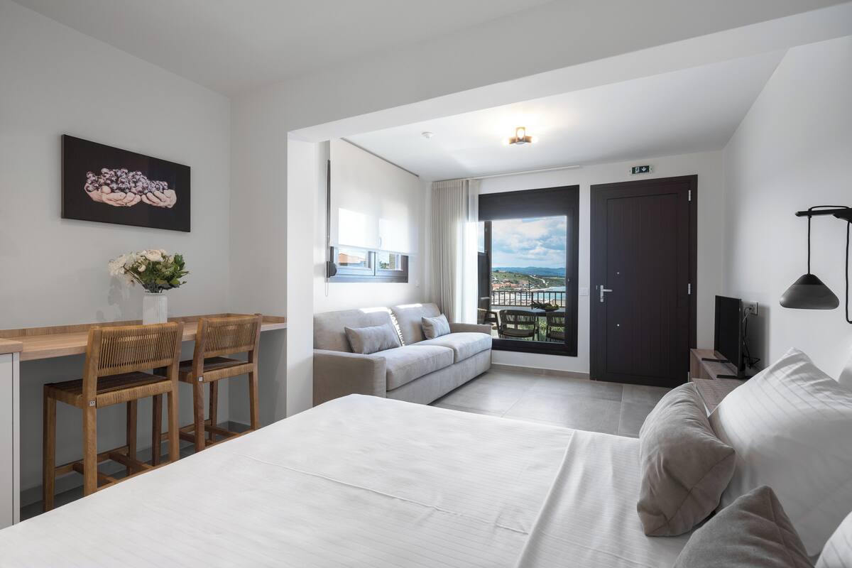Een moderne hotelkamer met een groot bed, een bank, een bureau met stoelen, een televisie en een balkon met uitzicht.