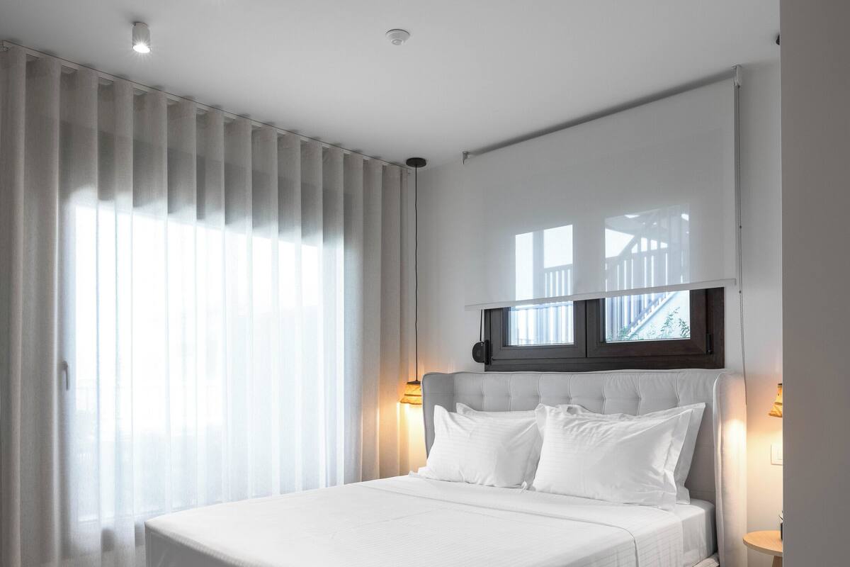 Een moderne slaapkamer met een groot bed, een raam met zonwering en een plafondlamp.