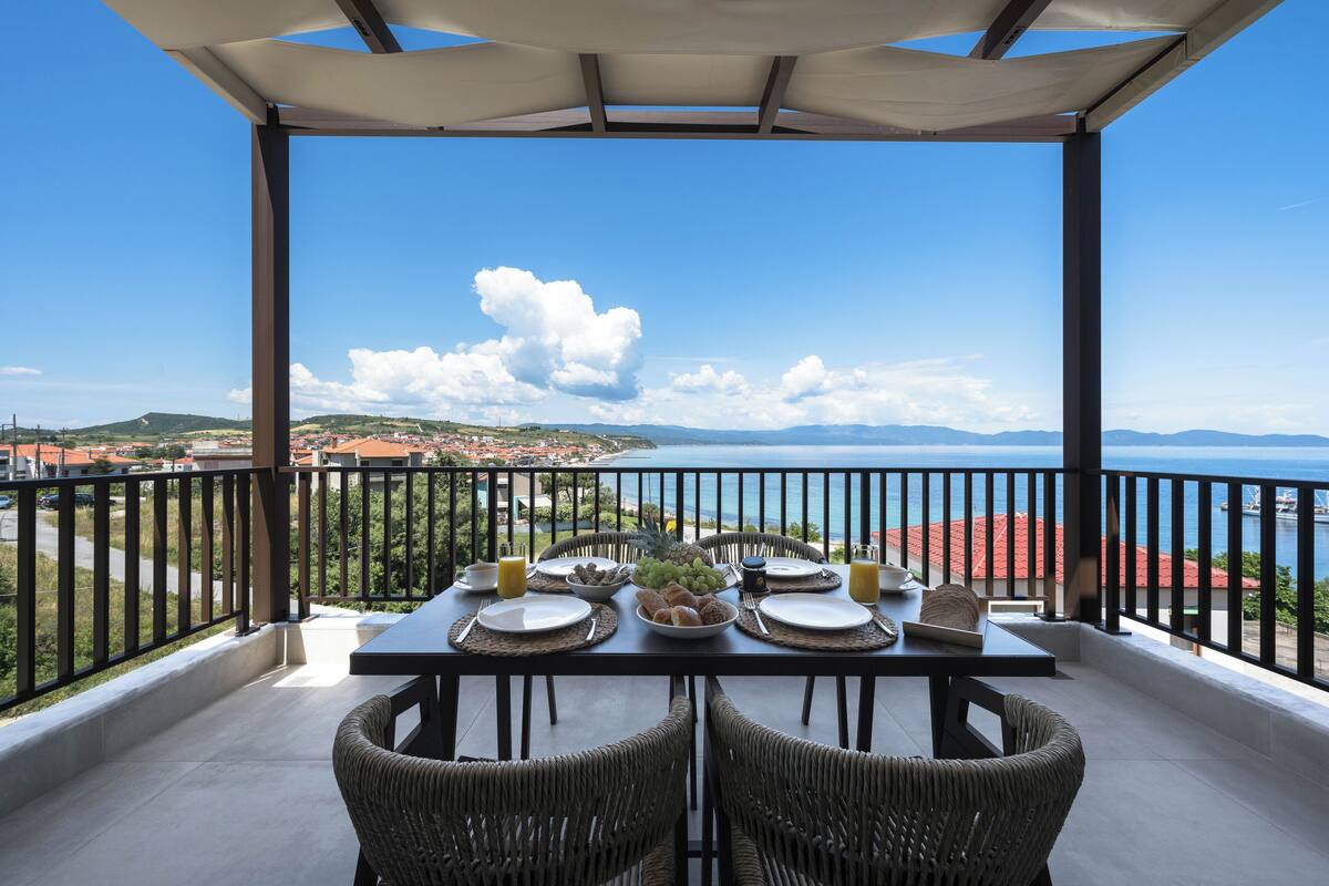 Een balkon met een tafel gedekt voor twee personen, met uitzicht op een pittoresk kustplaatsje en de zee.