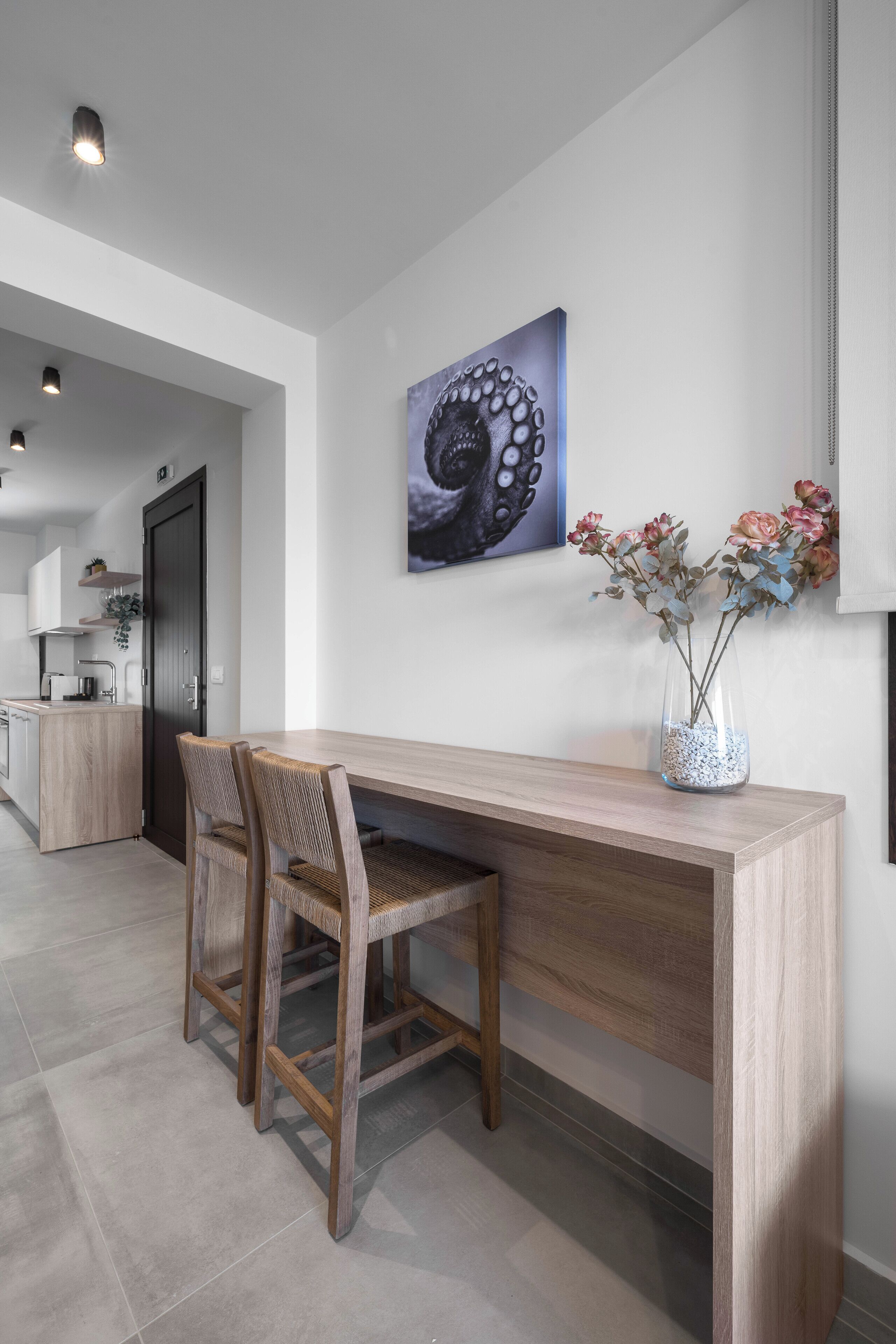 A modern kitchen with a wooden island, a dining area with a long table and chairs, and a wall-mounted painting.