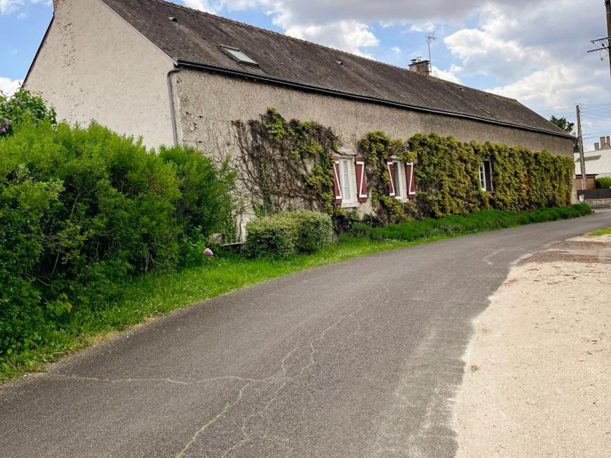 A narrow, paved road curving alongside a building with a sloped roof and red-framed windows, surrounded by lush greenery.