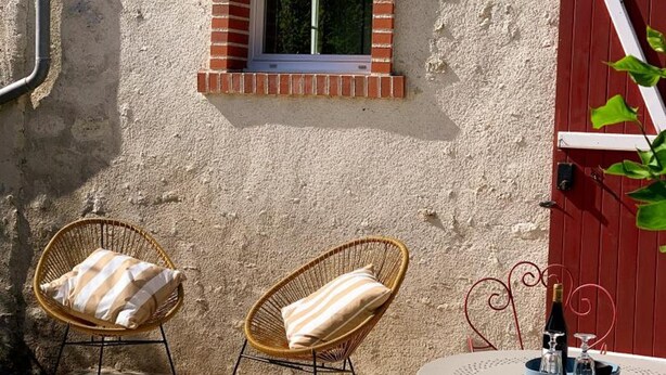 Eine Terrasse mit zwei Korbstühlen, einem kleinen Tisch mit Flasche und Glas sowie einer roten Tür.