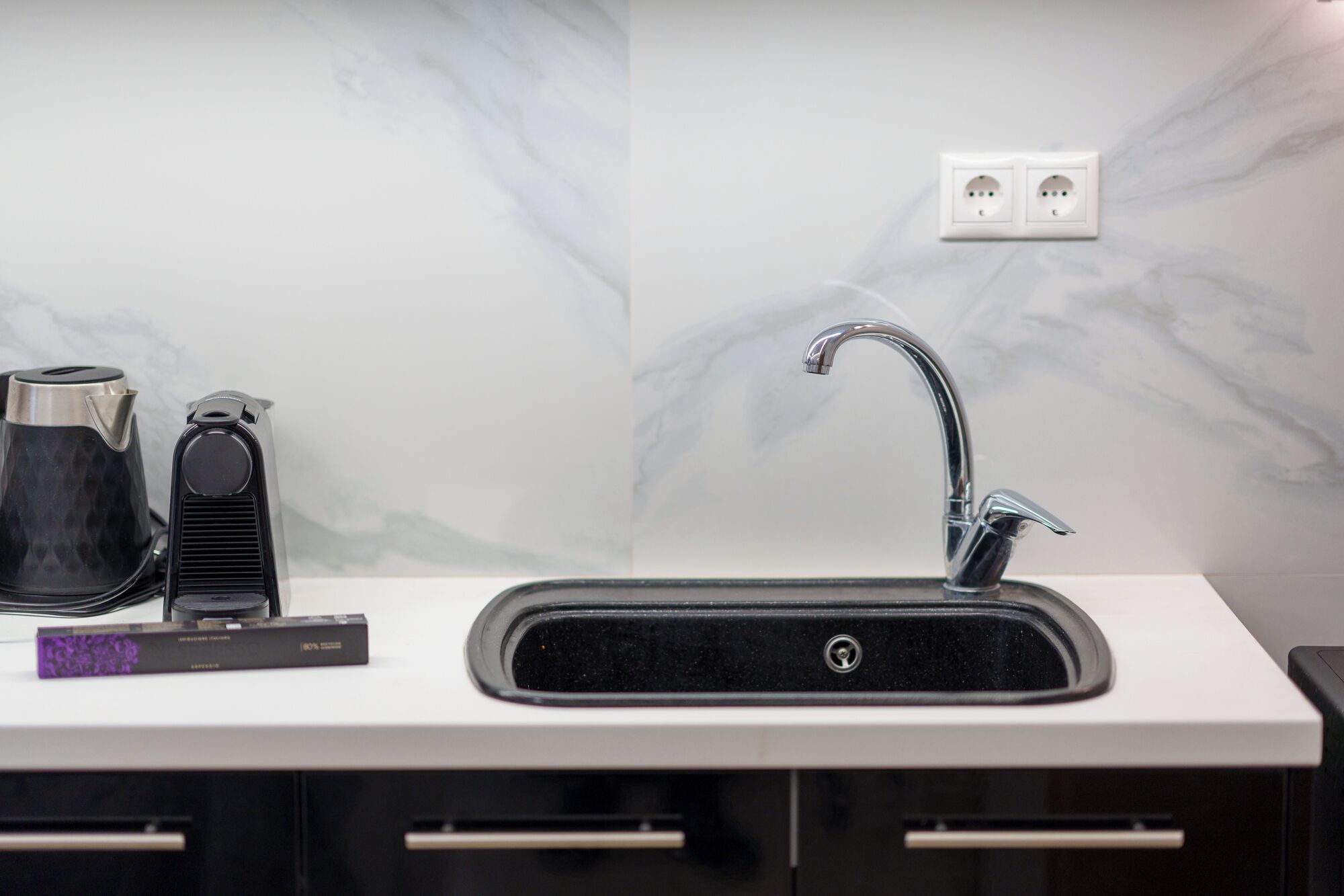 A modern kitchen with a black sink, a coffee maker, and a power strip on the countertop.