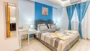 Ein Schlafzimmer mit Bett, Nachttischen, Schreibtisch, blauer Wand und einem Fenster mit Vorhängen.