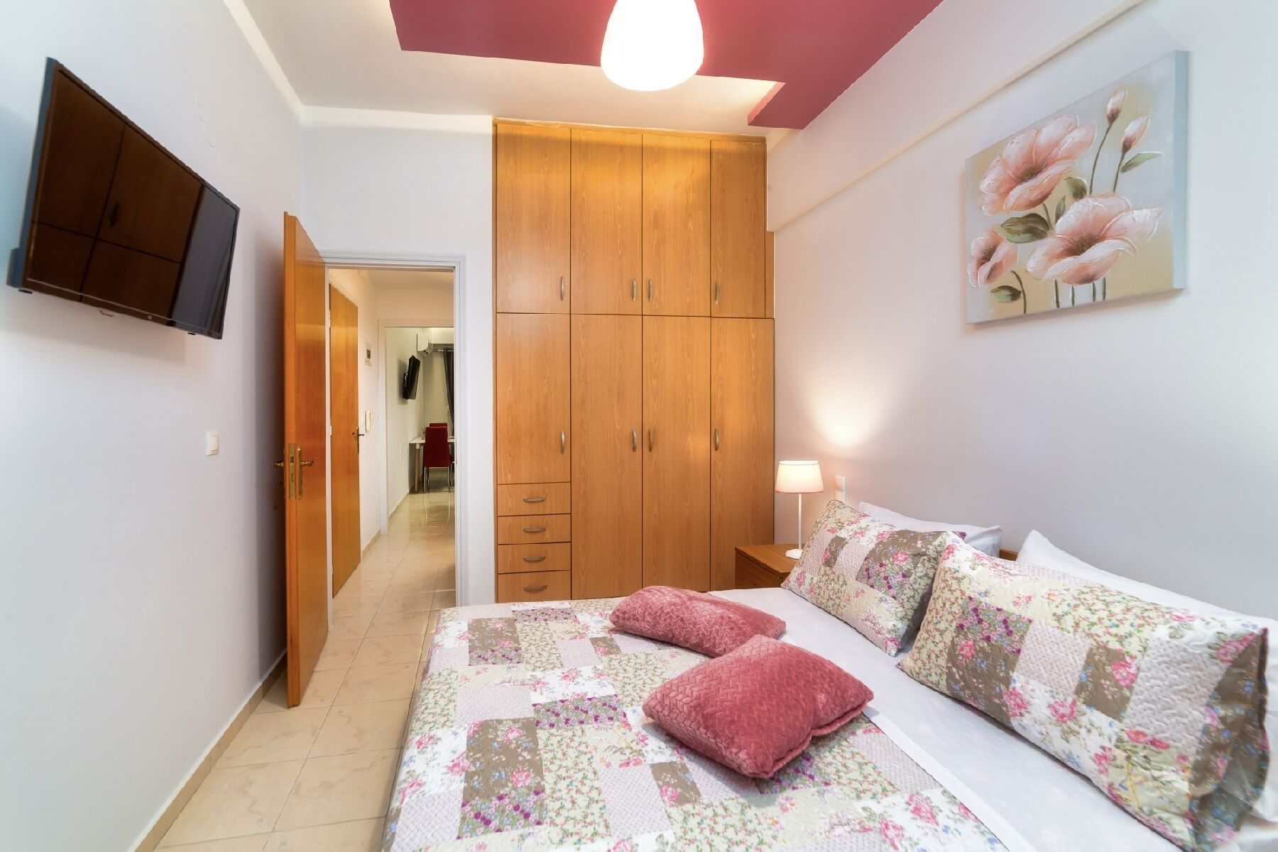 Een slaapkamer met een bed, een kledingkast, een schilderij en een televisie aan de muur.