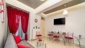 Ein modernes Wohnzimmer mit einem grauen Sofa, roten Kissen, einem Glastisch und einem Essbereich mit einem Tisch und Stühlen.