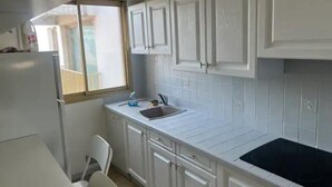 A compact kitchen with white cabinets, a black stove, and a window providing natural light. - Spacieux et Lumineux T2 au Cœur de Biarritz Proche e la Plage + Parking Privatif (Biarritz)