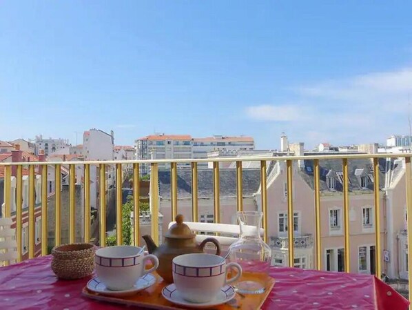 A balcony with a table set for tea, overlooking a cityscape.