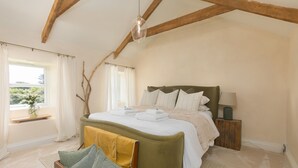 Un dormitorio con cama, mesita de noche, lámpara, ventana con cortinas y vistas a zonas verdes.