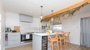 Una cocina moderna con armarios blancos, horno empotrado, lavabo y taburetes de madera.