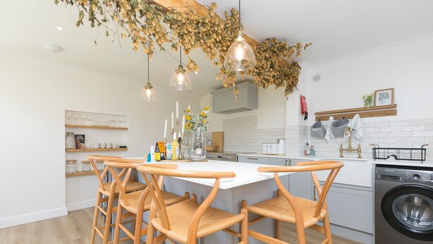Una cocina moderna con una isla central, sillas de madera, luces colgantes y una lavadora.