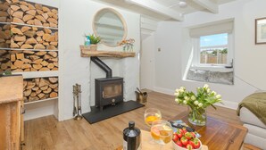 Una sala de estar acogedora con un estufa de leña, una chimenea, un estante de madera con leños, un espejo redondo y un ventanal.