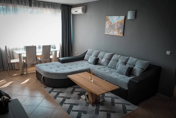 A modern living room with a sectional sofa, a wooden coffee table, and a dining area with chairs and a table. - Apartment - Sleeps 4 & Free Parking (Nessebar)