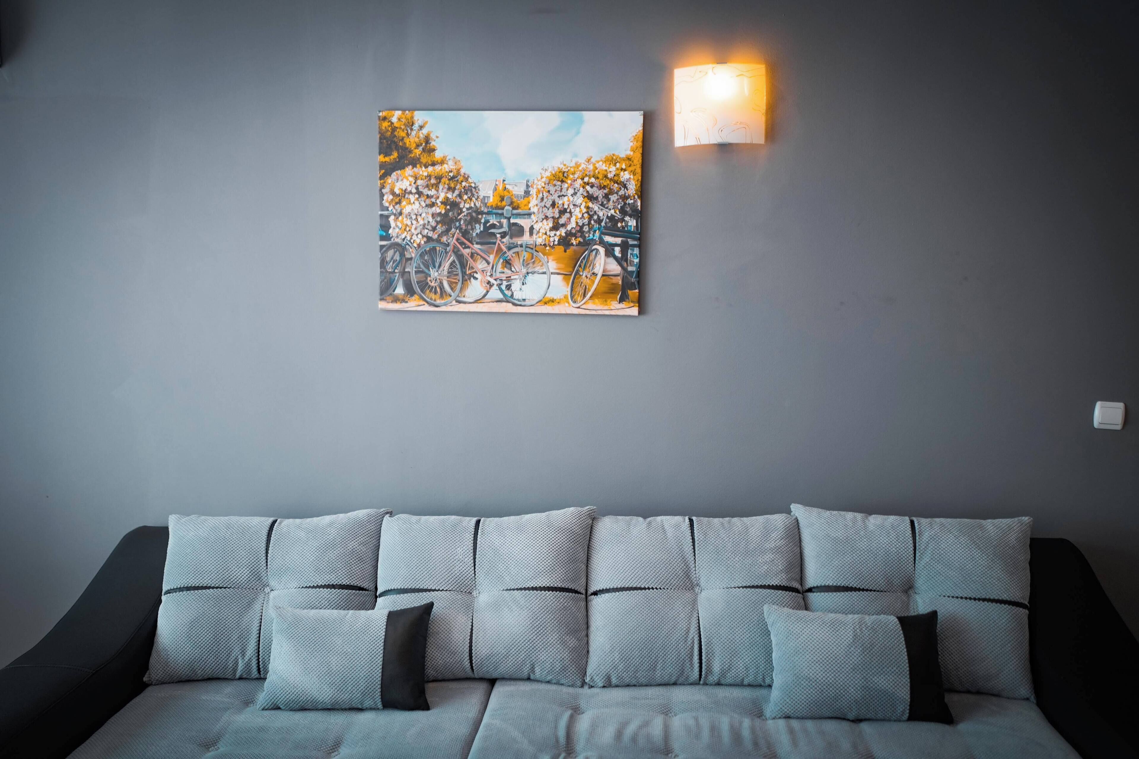 Ein modernes Wohnzimmer mit einem grauen Sofa, einem Wandbild mit Fahrrädern und einer Wandleuchte.