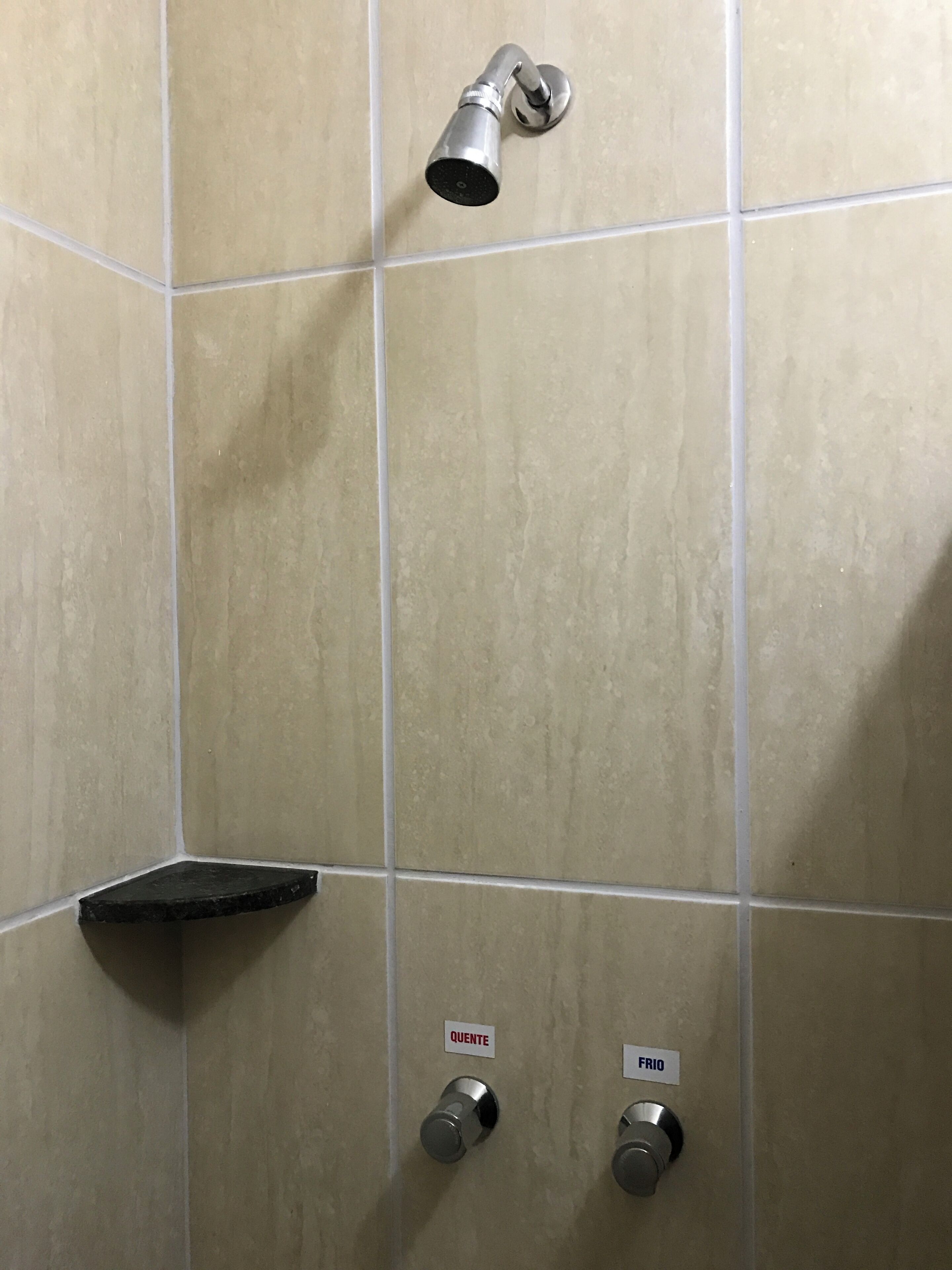 Ein Duschbereich mit Handbrause, Ablagefläche in Schwarz und zwei Bedienelementen, beschriftet mit 'QUENTE' und 'FRIO'.