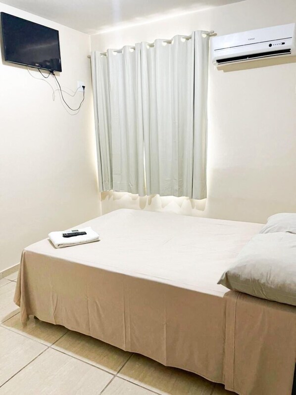 Habitación de hotel con cama, televisor de pantalla plana montado en la pared y aire acondicionado sobre la ventana.