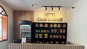Een hotel receptie met een marmeren balie, een etalage met snacks en een bordje met de tekst 'HOTEL CASA GRANDE'.