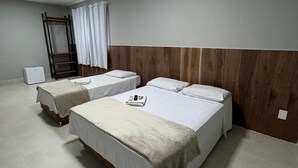 Een hotelkamer met twee eenpersoonsbedden, een houten hoofdbord, een airconditioner, een bureau met stoel, een kledingkast en een raam met gordijnen.