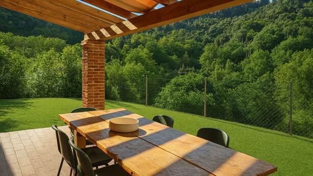 A wooden table with chairs under a pergola, set on a patio with a view of a forested hillside.