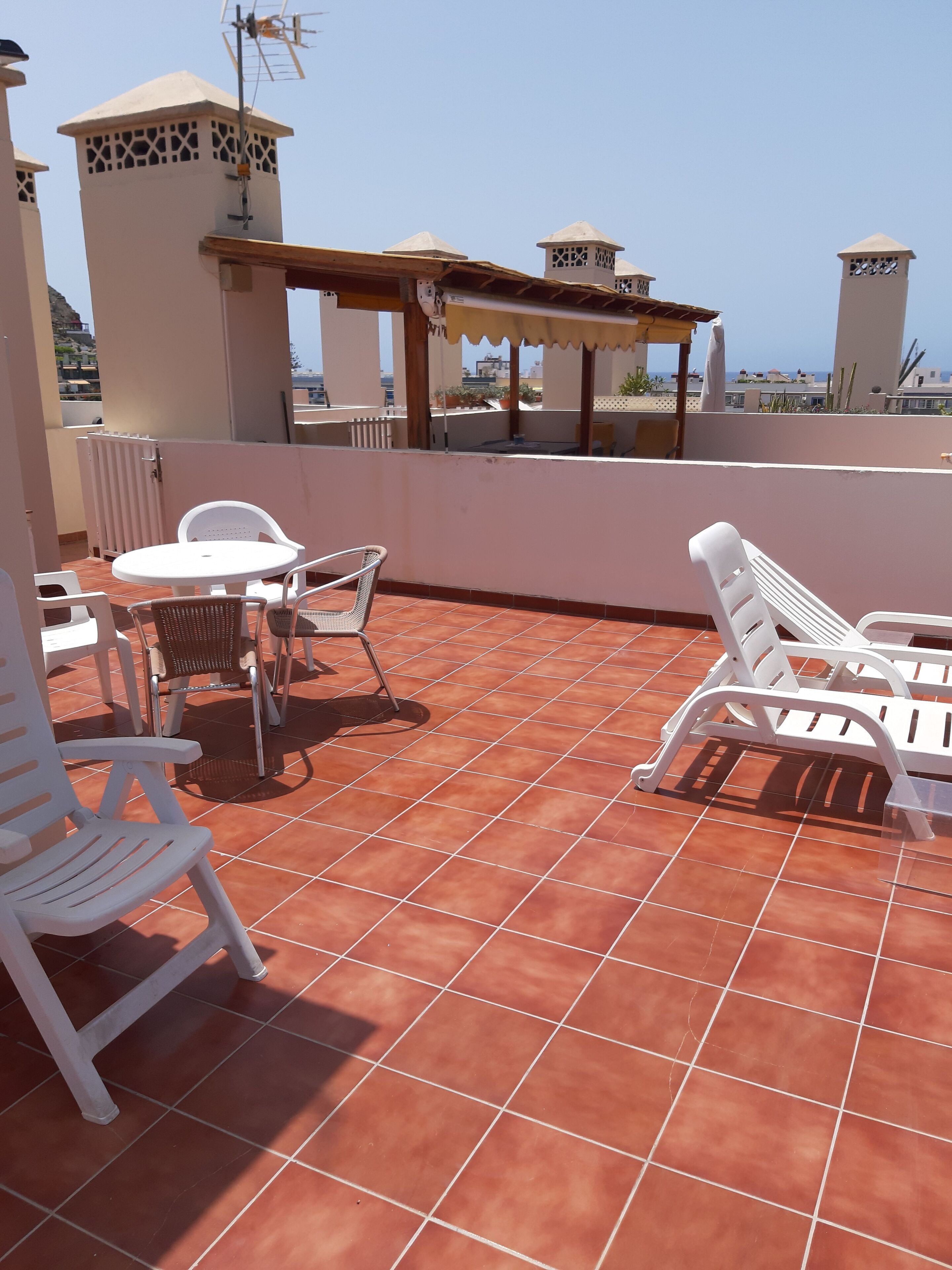 Una terrazza sul tetto con sedie e tavolo in plastica bianca, piastrelle in terracotta e vista sul mare.