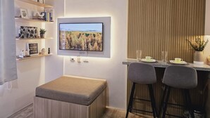 Ett modernt vardagsrum med en platt-TV som  är monterad på väggen, en liten sittgrupp med en vadderad bänk och två barstolar samt en väggpanel i trä.