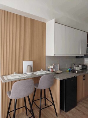 A modern kitchen with a wooden accent wall, two bar stools, a built-in dishwasher, and a countertop with various kitchen items.