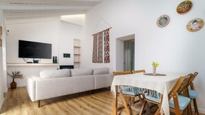 A modern living room with a sofa, a TV, and a dining area with a table and chairs. - Cottage in Aljezur- 2 bed Ensuite-casinha da Ivone (Aljezur)