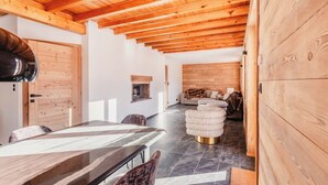 Un interno moderno con soffitto in legno, una zona pranzo con tavolo in marmo e un angolo salotto accogliente con poggiapiedi rotondo.